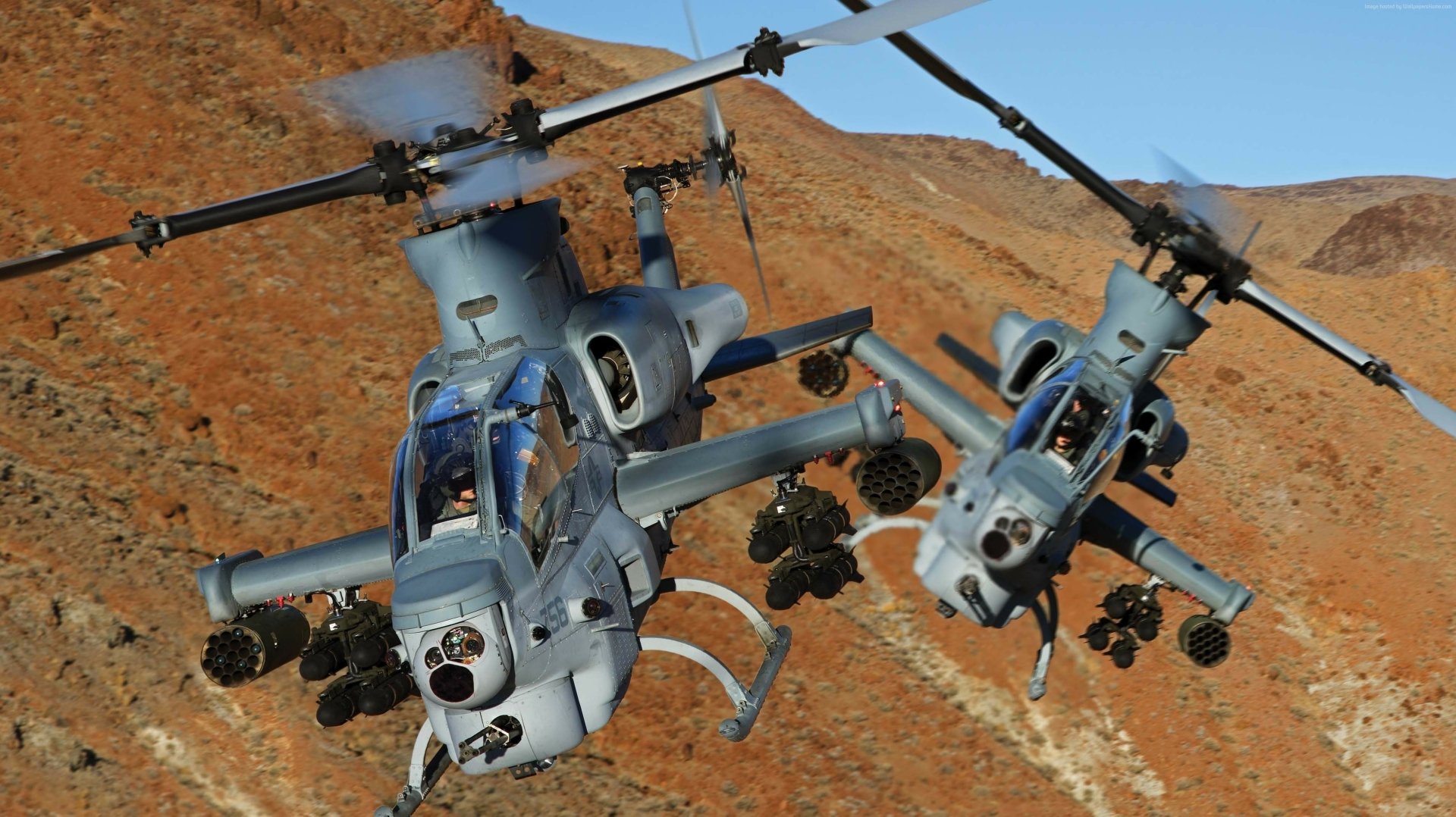 Two Bell AH-1Z Viper military helicopters fly over a rocky, mountainous desert landscape in this HD desktop wallpaper.