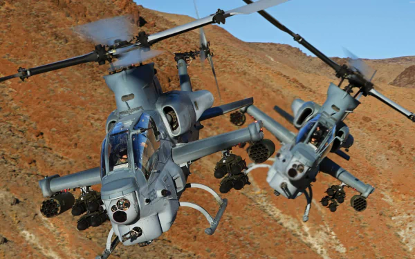 Two Bell AH-1Z Viper military helicopters fly over a rocky, mountainous desert landscape in this HD desktop wallpaper.