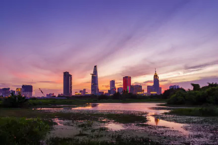 Evening skyline of Ho Chi Minh City, Vietnam, featuring the Bitexco Financial Tower. The vibrant sunset reflects over a serene water landscape, captured in HD for a striking desktop wallpaper.