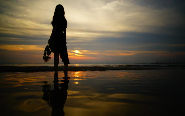 Silhouette of a woman standing at the beach, reflecting on the water during a vibrant sunset. An 8K Ultra HD wallpaper capturing serene beauty and tranquility.