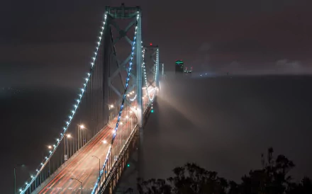 Night view of San Francisco’s Bay Bridge illuminated through fog, captured as an HD PC desktop wallpaper with glowing lights and a misty atmosphere.
