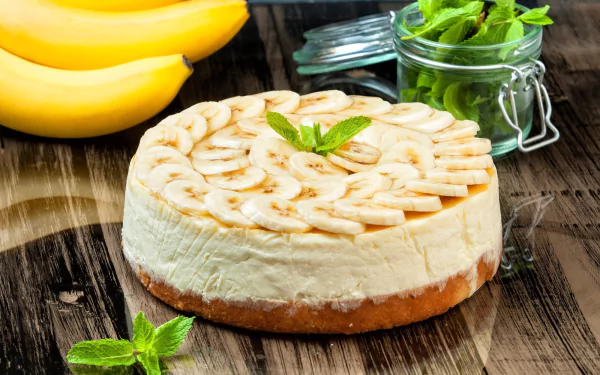 HD desktop wallpaper showcasing a banana pastry cake garnished with fresh mint on a wooden surface, accompanied by whole bananas and a jar of mint leaves.