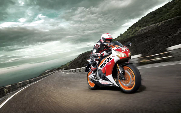 HD desktop wallpaper showing a Honda CBR1000RR motorcycle speeding on a winding road against a dramatic cloudy sky and rocky hillside background.