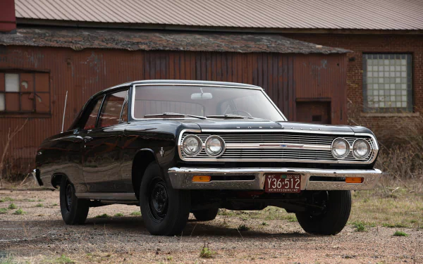 HD PC desktop wallpaper showing a black Chevrolet Chevelle muscle car parked before a weathered barn, a classic Chevrolet vehicle with chrome grille and vintage styling.