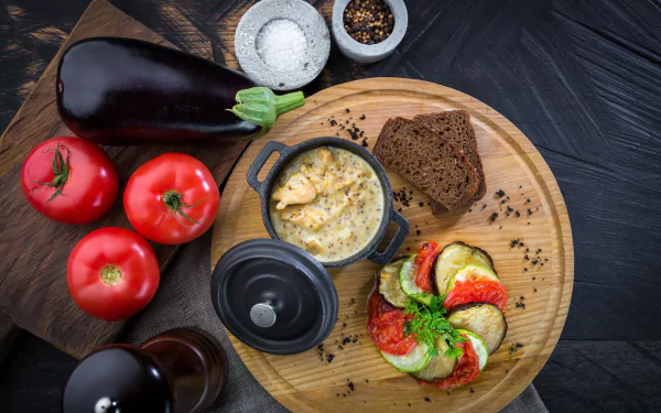 HD PC desktop wallpaper still life: eggplant and tomatoes with baked gratin, sliced zucchini and dark bread on a wooden board — food arranged as a rustic background.