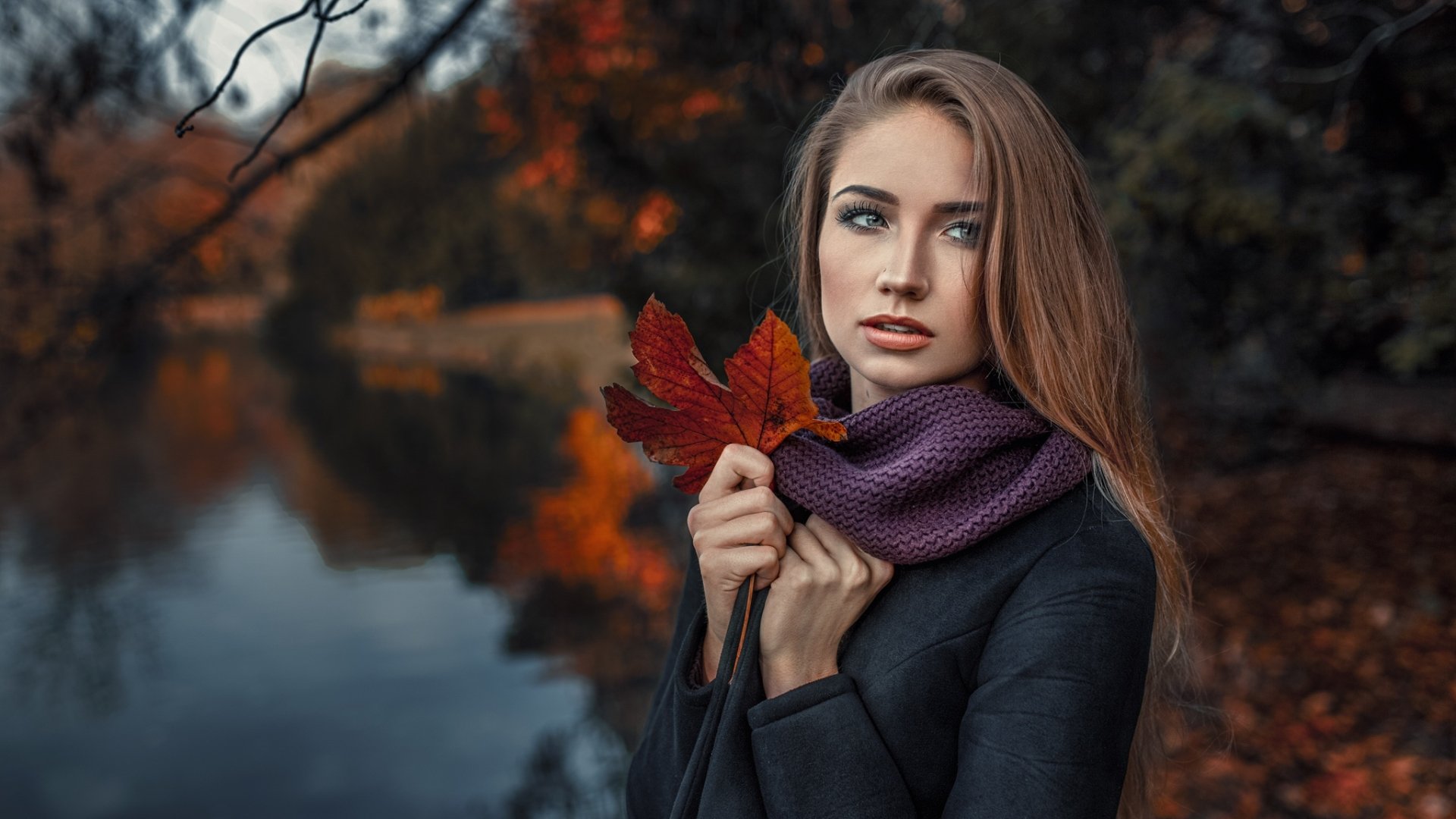 HD PC desktop wallpaper: brunette model with blue eyes in a purple scarf holds a red fall leaf by a lakeside, autumn colors and shallow depth of field.
