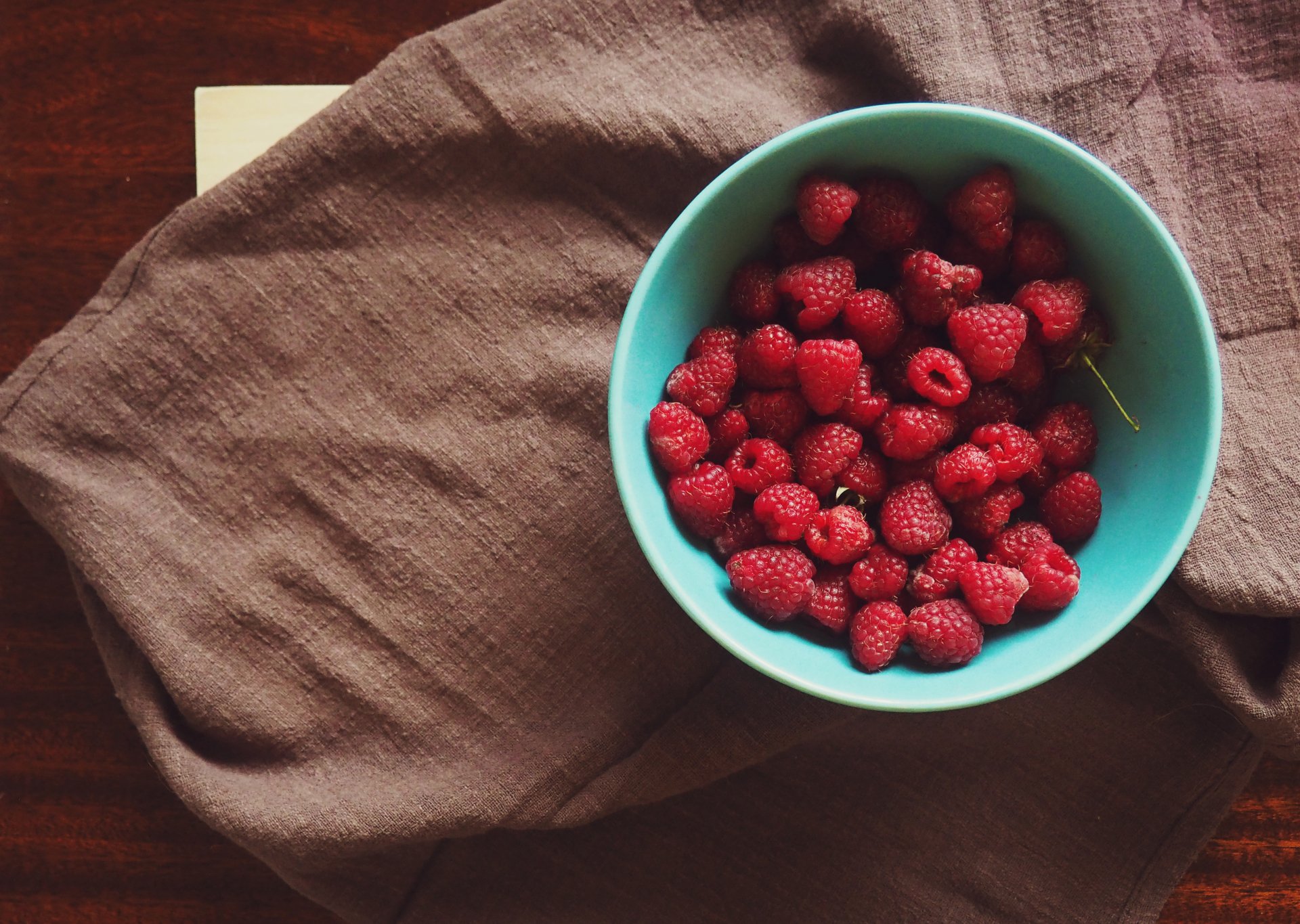 HD wallpaper of a bowl filled with fresh raspberries atop a rustic table with a linen cloth.