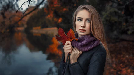 HD PC desktop wallpaper: brunette model with blue eyes in a purple scarf holds a red fall leaf by a lakeside, autumn colors and shallow depth of field.