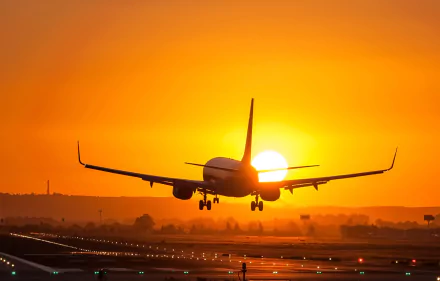 Passenger plane landing at sunrise with the sun glowing behind, captured in a vibrant HD desktop wallpaper showcasing the aircraft and warm sky.