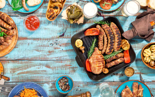 5K Ultra HD PC desktop wallpaper and background: a food still life of grilled sausages and assorted meats with sides, sauces and bread on a rustic blue table.