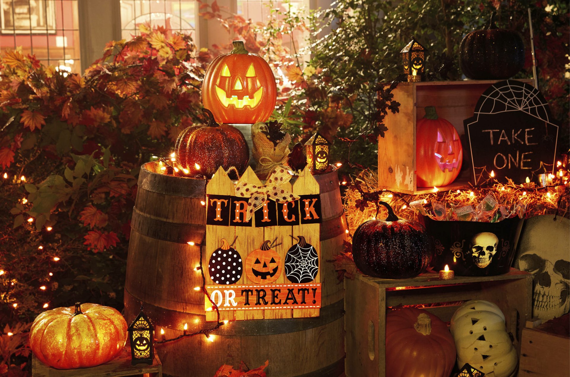 HD PC desktop wallpaper featuring a festive Halloween holiday scene with glowing jack-o'-lanterns, pumpkins, candy, and warm string lights in an autumn setting.