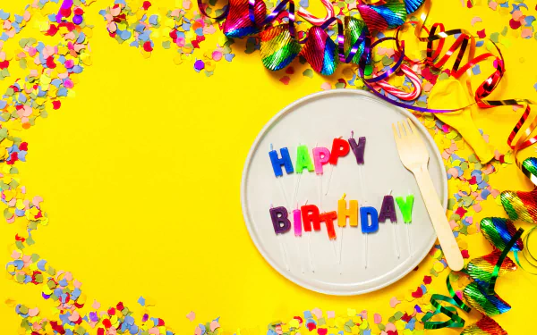 Colorful Happy Birthday candles on a white plate with vibrant confetti and ribbons on a bright yellow background. Festive celebration desktop wallpaper and background in HD.
