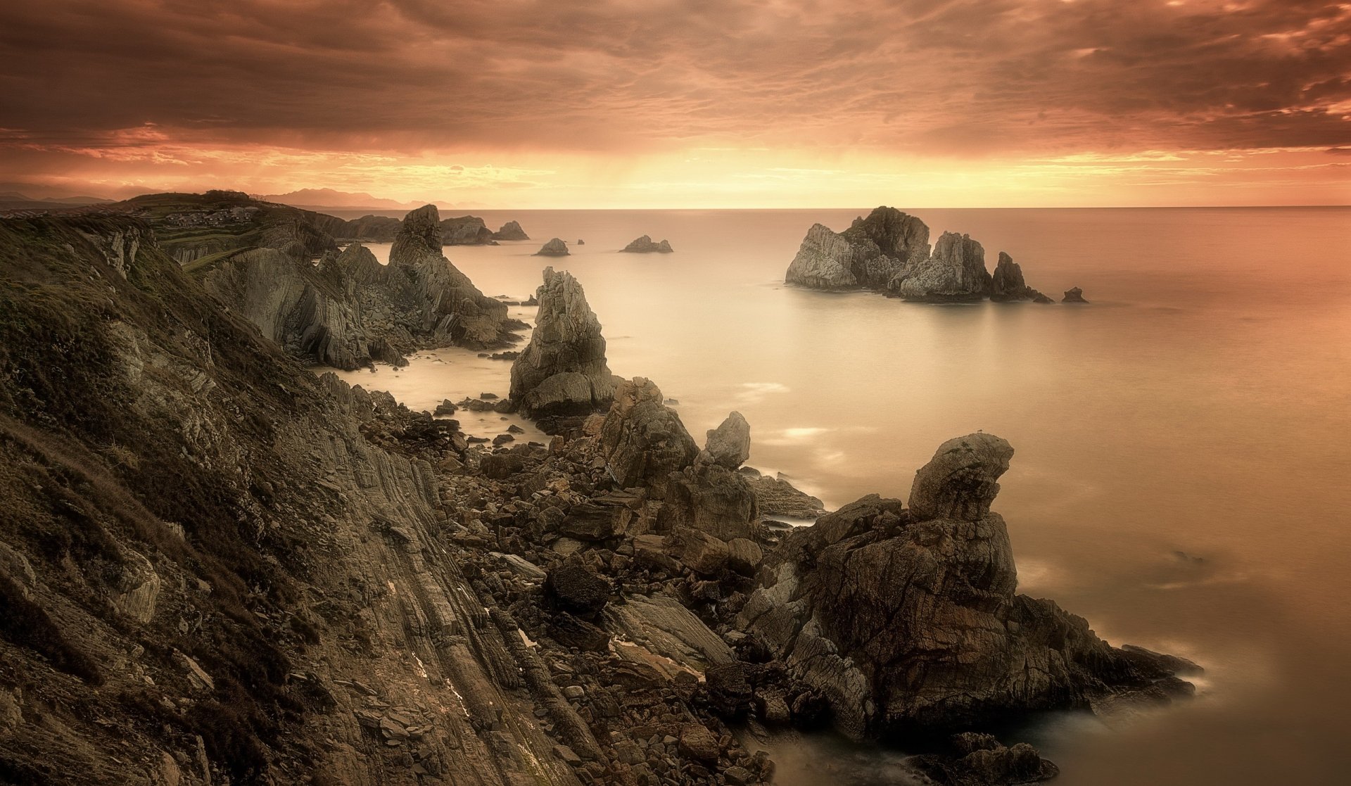 Sepia-toned HD desktop wallpaper of a rocky coastline under cloudy skies with the ocean stretching to the horizon, capturing nature’s serene beauty.