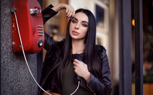 Model with long black hair and blue eyes poses holding a red wall telephone; shallow depth of field, polished portrait styled as a 2K Quad HD PC desktop wallpaper and background.