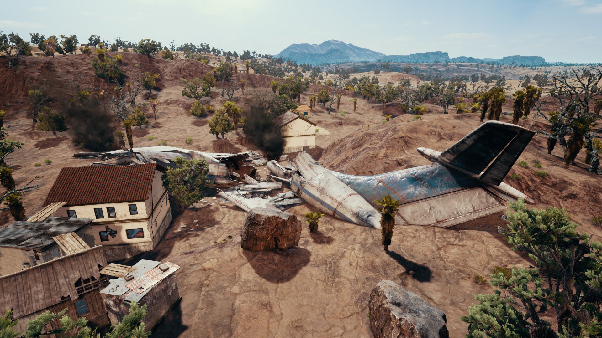 HD desktop wallpaper featuring a scene from the video game Playerunknown's Battlegrounds, depicting a crashed airplane in a rocky, desert-like area with surrounding buildings and trees.