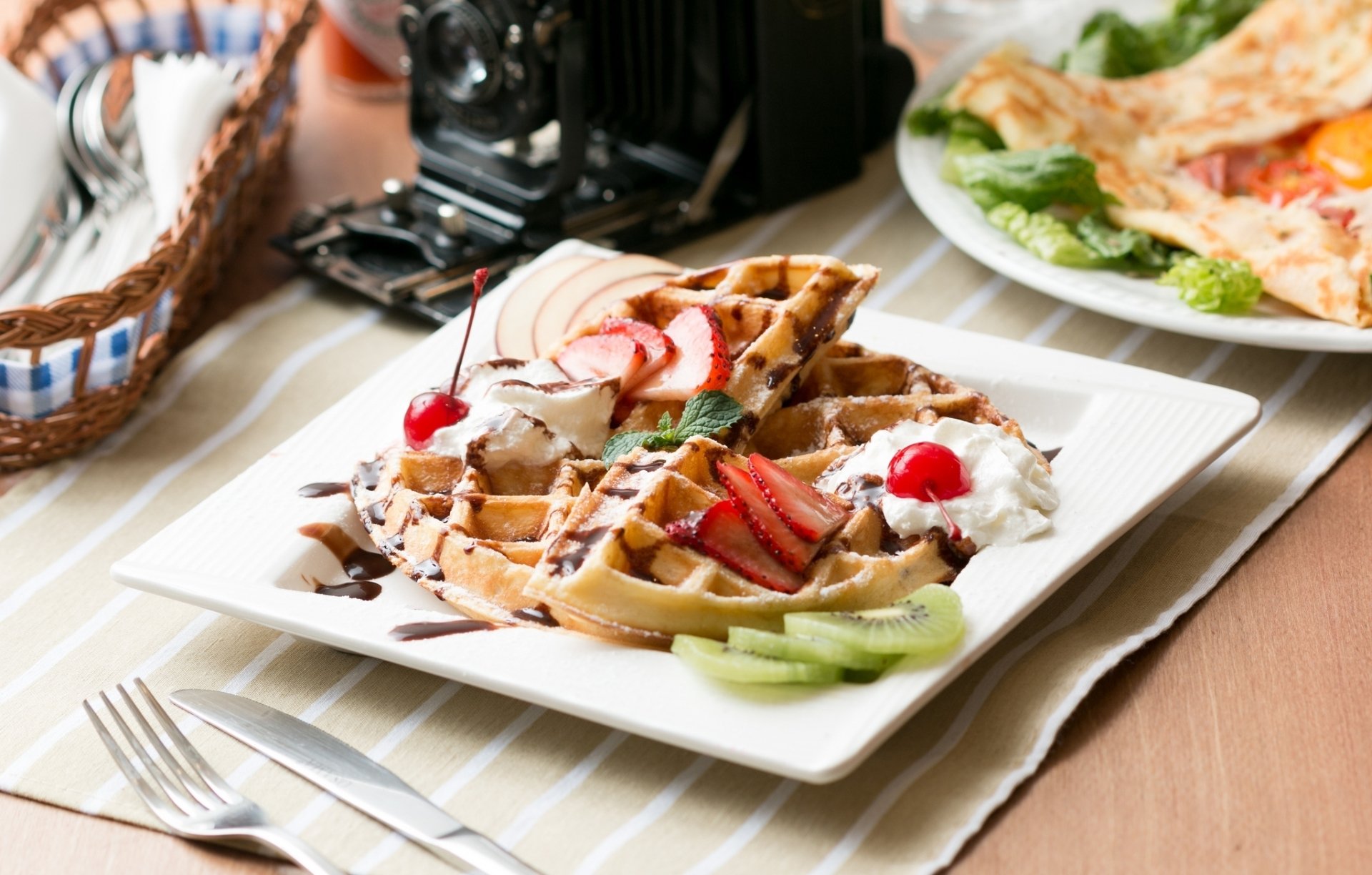 HD PC desktop wallpaper background of breakfast food: a golden waffle topped with strawberries, whipped cream, chocolate drizzle and cherries.