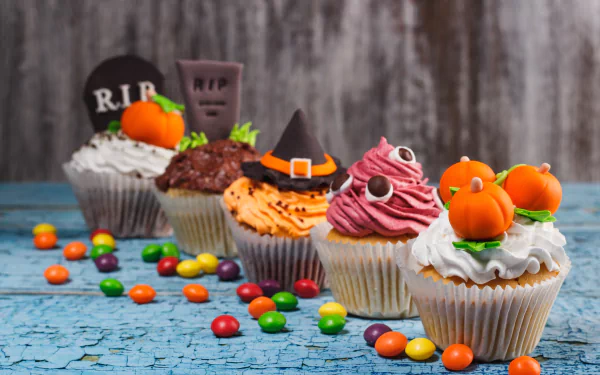 A vibrant 4K Ultra HD Halloween-themed cupcake lineup with colorful cream frosting, candy decorations, and spooky edible tombstones on a rustic blue wooden surface.