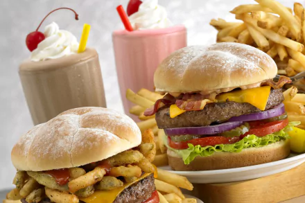 HD desktop wallpaper featuring two burgers with lettuce, tomato, cheese, onions, bacon, french fries, and milkshakes topped with whipped cream and cherries.