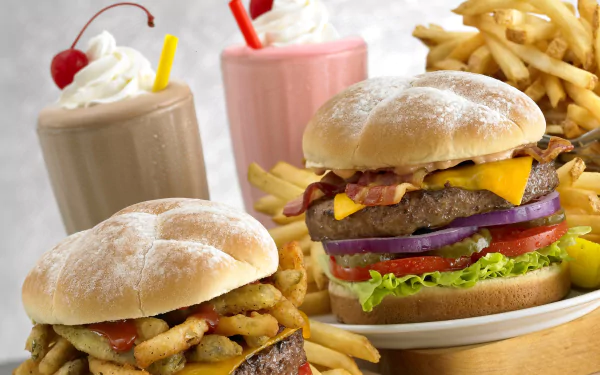 HD desktop wallpaper featuring two burgers with lettuce, tomato, cheese, onions, bacon, french fries, and milkshakes topped with whipped cream and cherries.