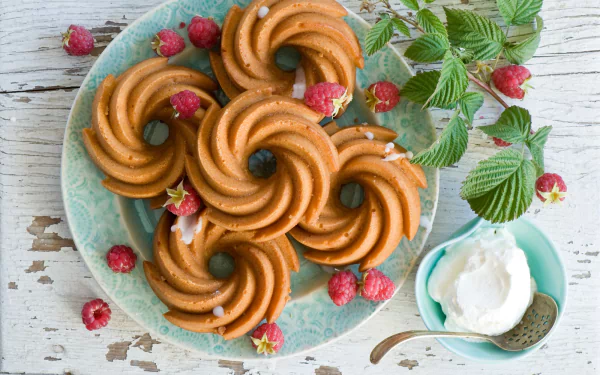 HD desktop wallpaper featuring a still life of spiral cookies and fresh raspberries on a blue plate with a small bowl of cream on a rustic wooden surface.