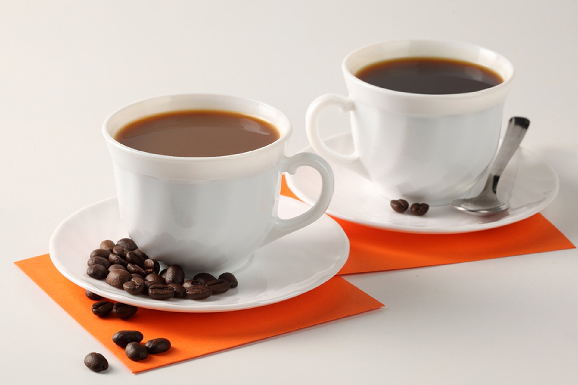 Two white cups filled with coffee, accompanied by coffee beans on white saucers and orange napkins, captured in 4K Ultra HD for a PC desktop wallpaper.
