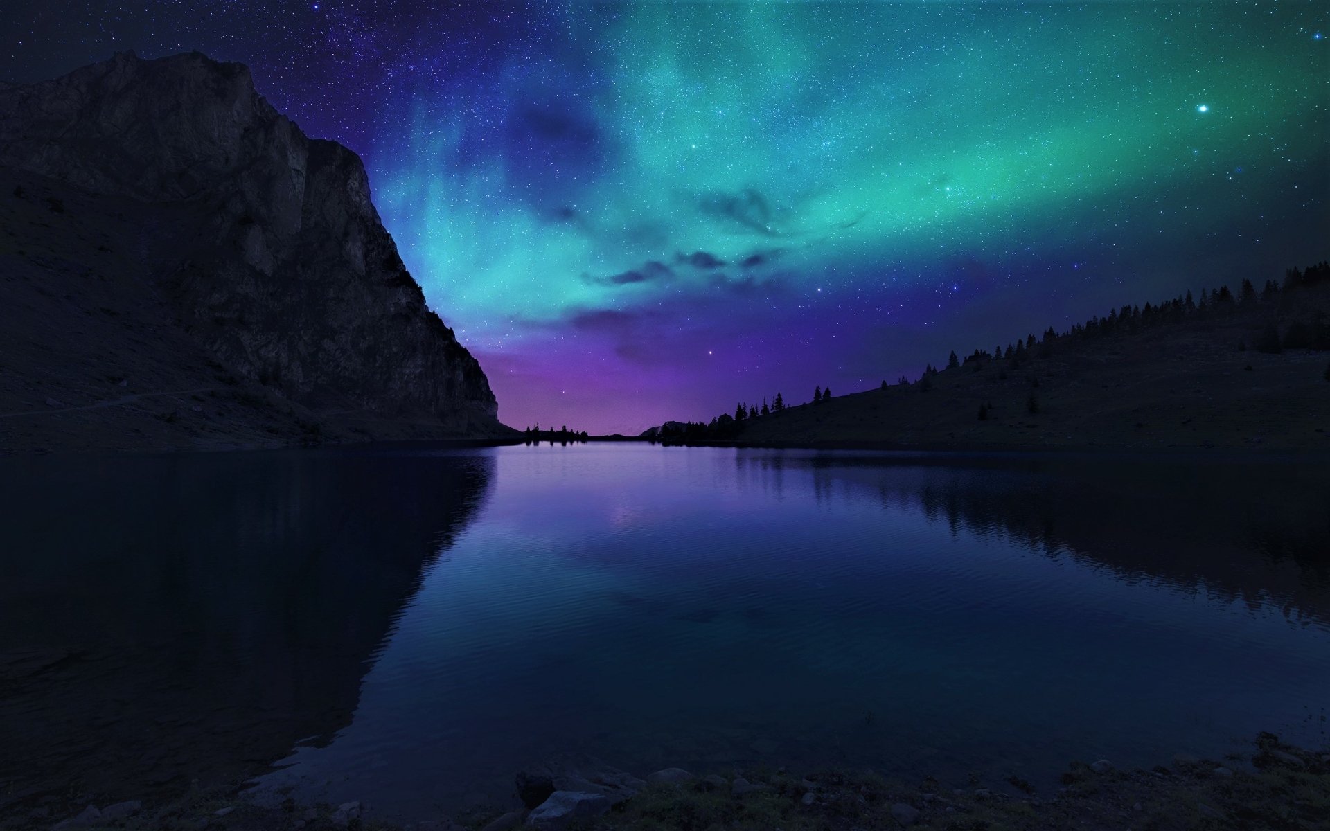 A HD desktop wallpaper showing a silhouette of a mountain and lake under a starry sky illuminated by the aurora borealis. The vibrant lights reflect on the calm water, creating a serene night scene.