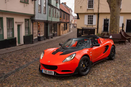 A vibrant red Lotus Elise sports car is parked on a cobblestone street in a historic town, captured in a high-definition desktop wallpaper background.