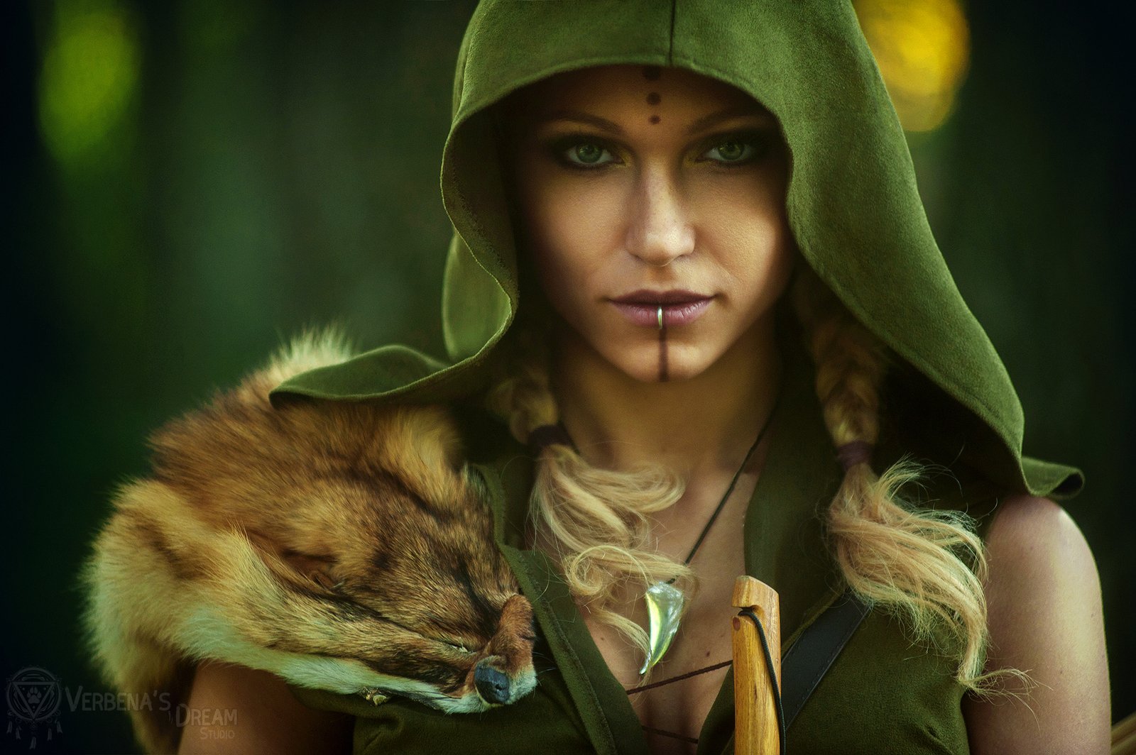 HD desktop wallpaper of a woman in detailed cosplay wearing a green hood, with face paint and a fur accessory, set against a blurred natural background.
