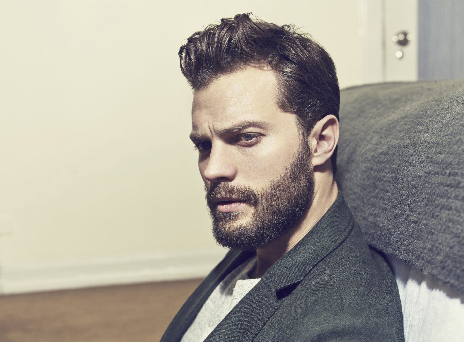 HD desktop wallpaper featuring Irish actor Jamie Dornan with a beard, seated and gazing thoughtfully.