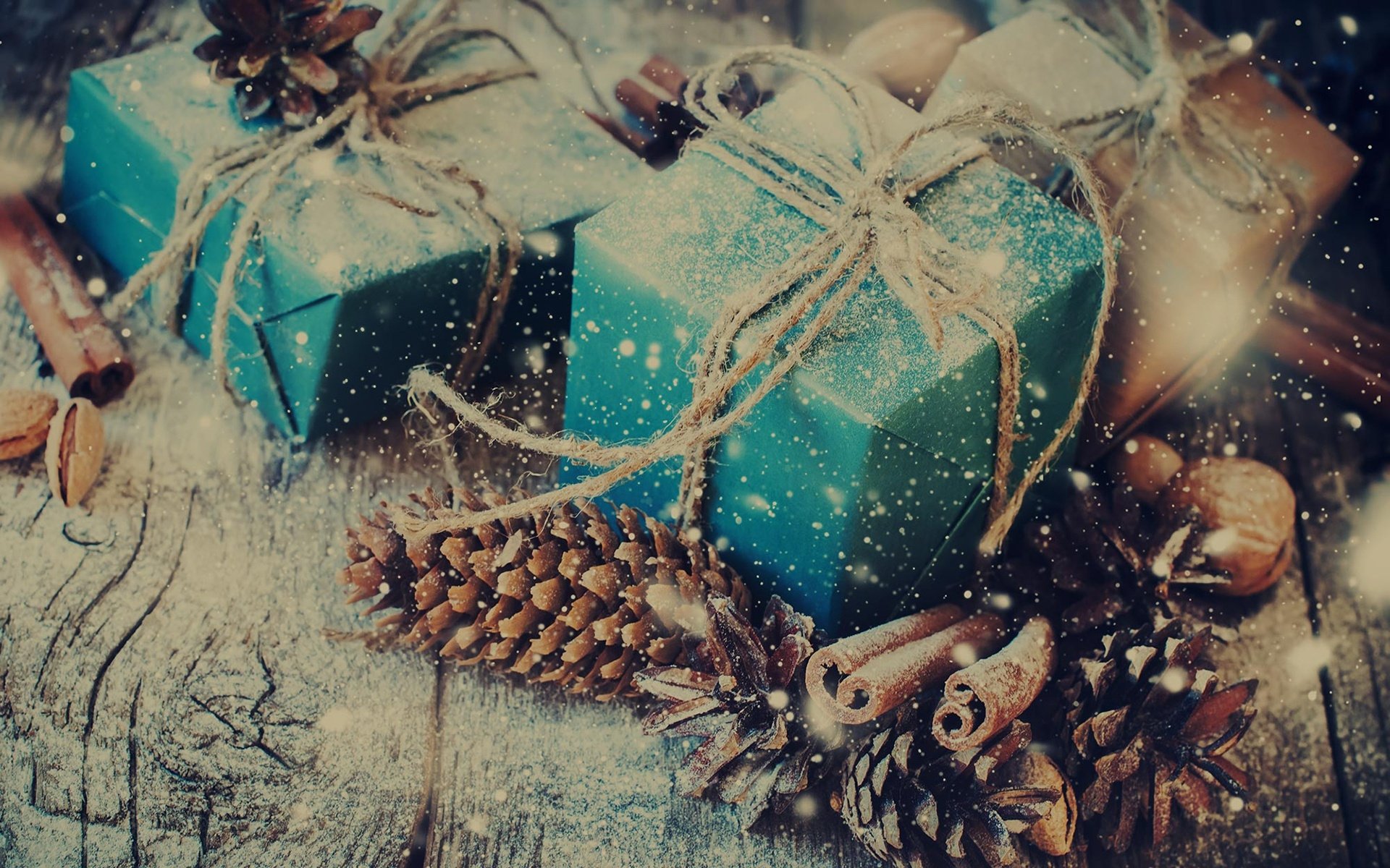 HD PC desktop wallpaper featuring cinnamon sticks, pine cones, and wrapped gifts arranged on a rustic wooden surface with a warm, festive atmosphere.