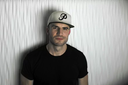 HD desktop wallpaper featuring a man in a cap and black shirt against a striped background.
