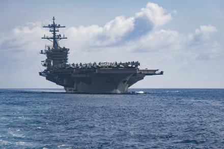HD wallpaper of the warship USS Theodore Roosevelt (CVN-71), an aircraft carrier, sailing in calm blue waters under a partly cloudy sky.