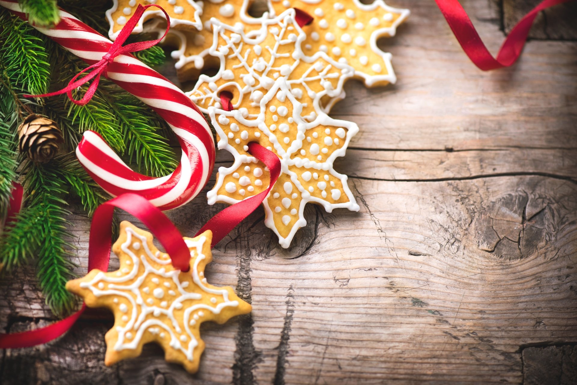 Festive Christmas-themed 4K Ultra HD wallpaper showing candy canes, decorated snowflake cookies, and evergreen branches on a rustic wooden background.