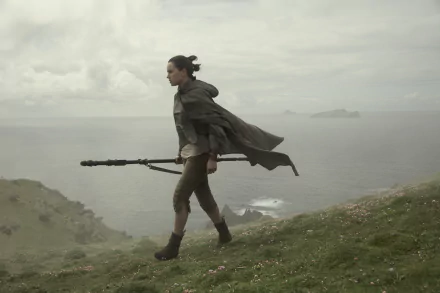 Daisy Ridley as Rey in a scene from Star Wars: The Last Jedi, walking along a cliffside with her staff, featured in a HD PC desktop wallpaper.