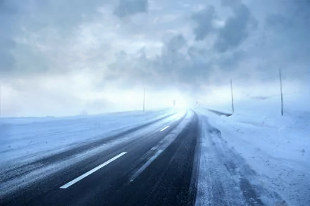 HD desktop wallpaper of a snow-covered road during a storm, with dark clouds overhead and a faint glow on the horizon.
