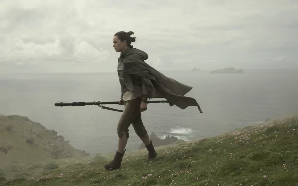 Daisy Ridley as Rey in a scene from Star Wars: The Last Jedi, walking along a cliffside with her staff, featured in a HD PC desktop wallpaper.