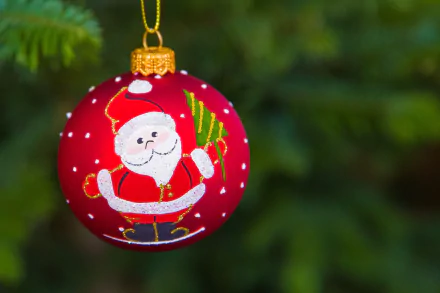A close-up of a red Christmas ornament featuring a smiling Santa Claus, hanging on a tree with a blurred green background, captured with depth of field for a festive HD desktop wallpaper.
