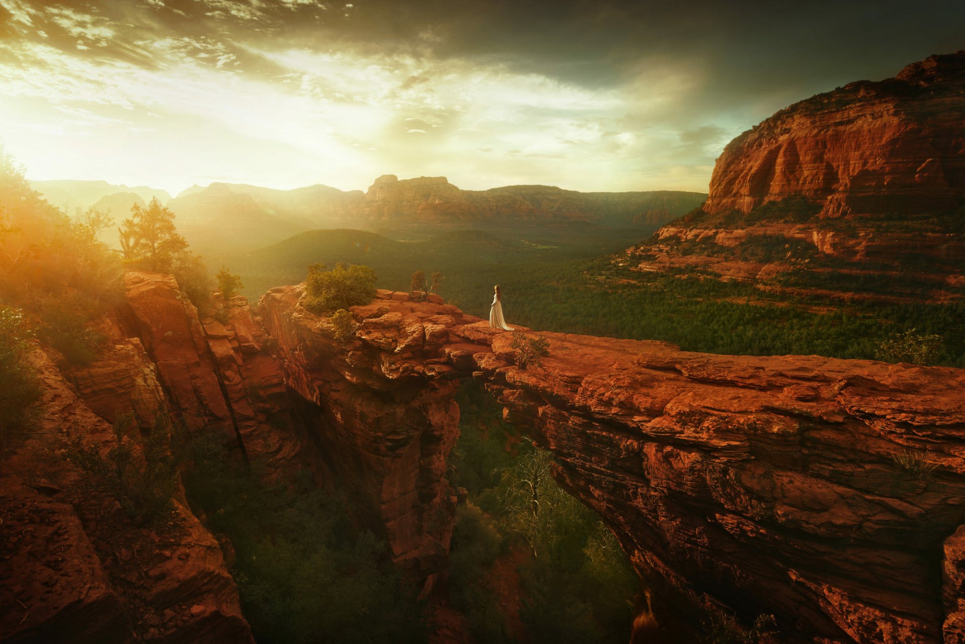 HD PC desktop wallpaper background showing a woman model in a flowing white dress standing on a red rock natural bridge at sunset overlooking a vast canyon.