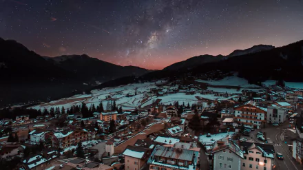 Winter night over a snowy mountain town beneath a starry sky, featuring the Milky Way stretching across a clear, dark night.