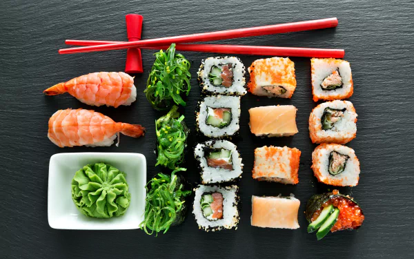 5K Ultra HD PC desktop wallpaper: still-life sushi spread—nigiri, maki, seaweed salad and wasabi with red chopsticks on slate, showcasing seafood, rice and fish.