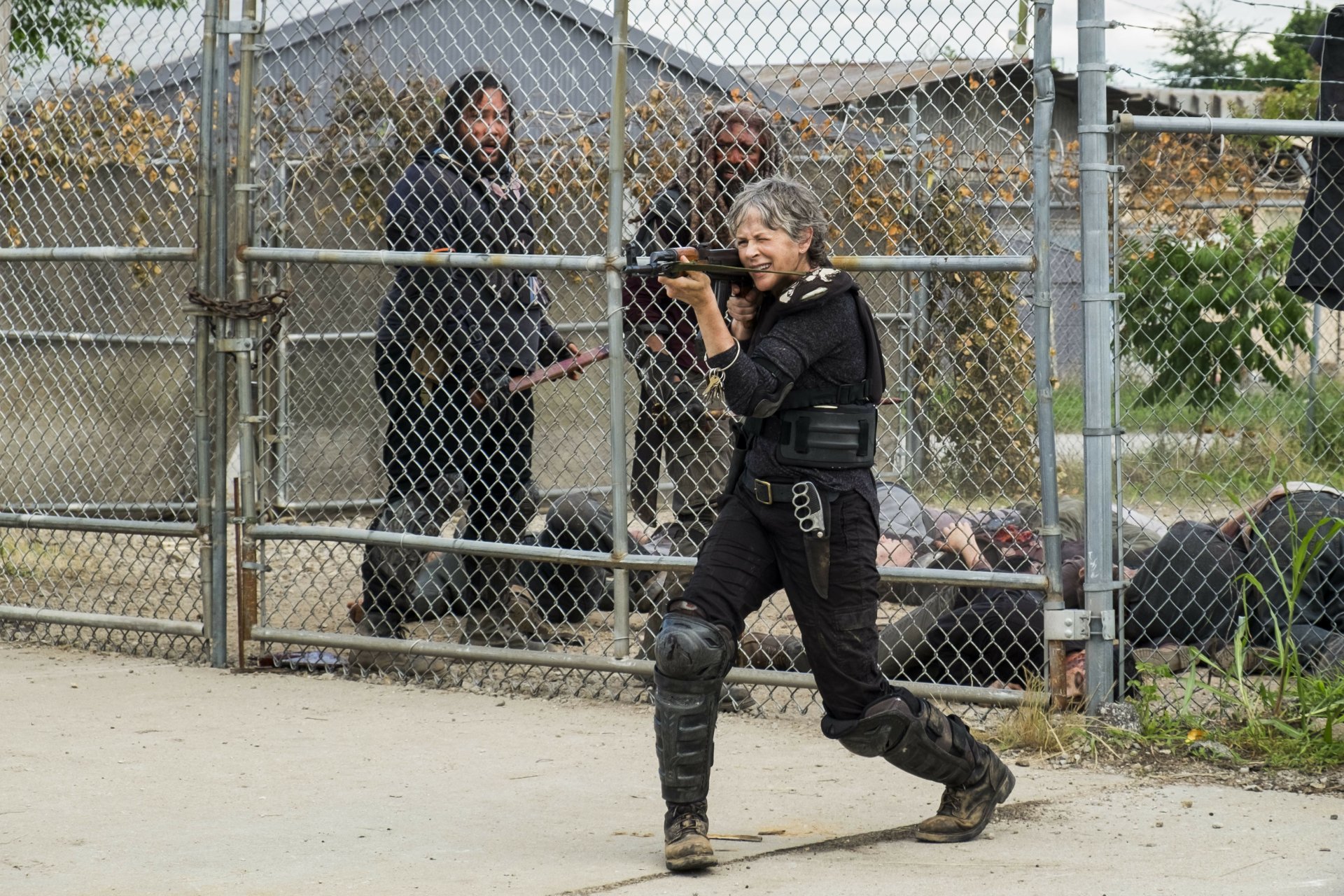 Ezekiel (Khary Payton) and Carol Peletier (Melissa Mcbride) from The Walking Dead walk near a chain-link fence in a 4K UHD TV show wallpaper.