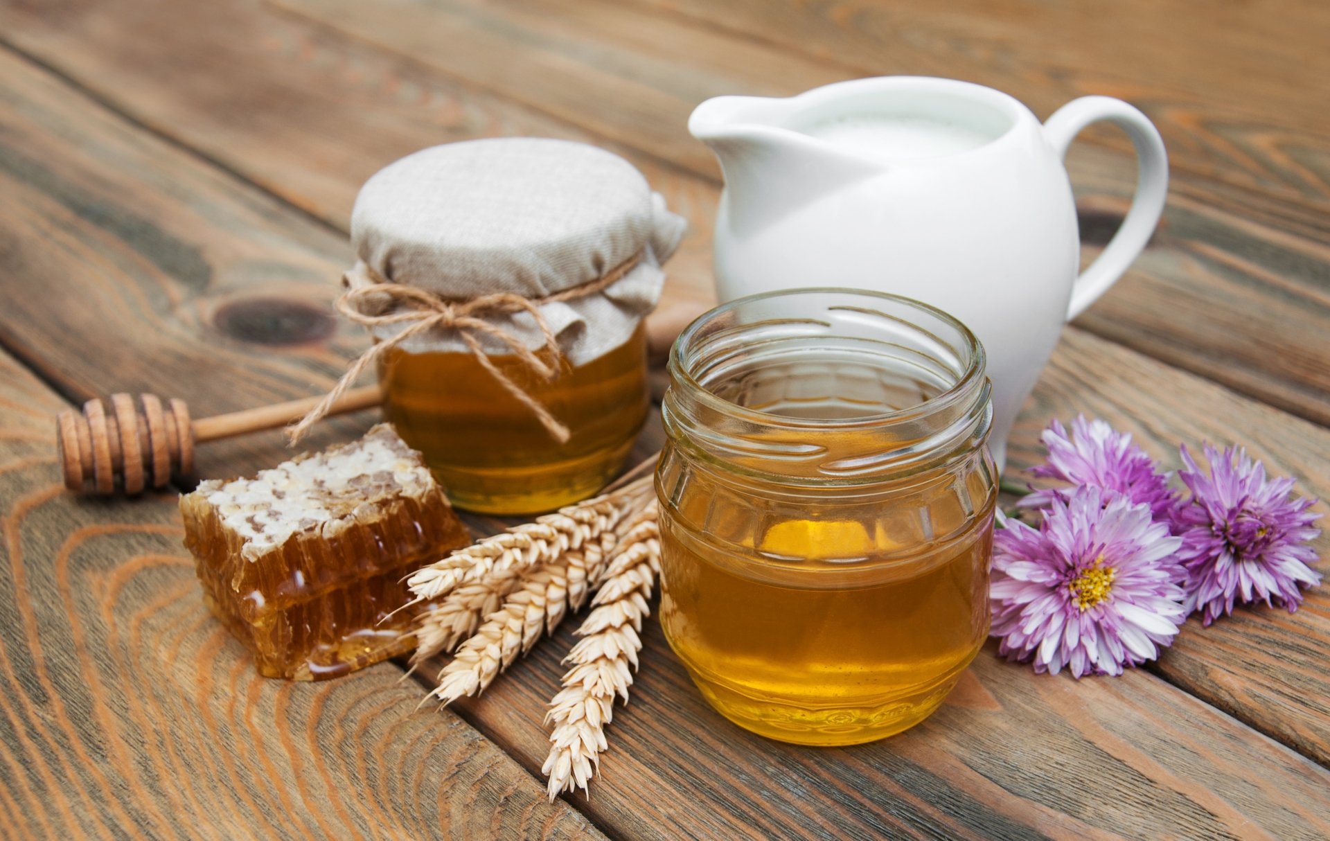 4K Ultra HD still life PC wallpaper featuring honey in a jar and honeycomb, a milk pitcher, wheat stalks, and purple flowers on a rustic wooden surface.