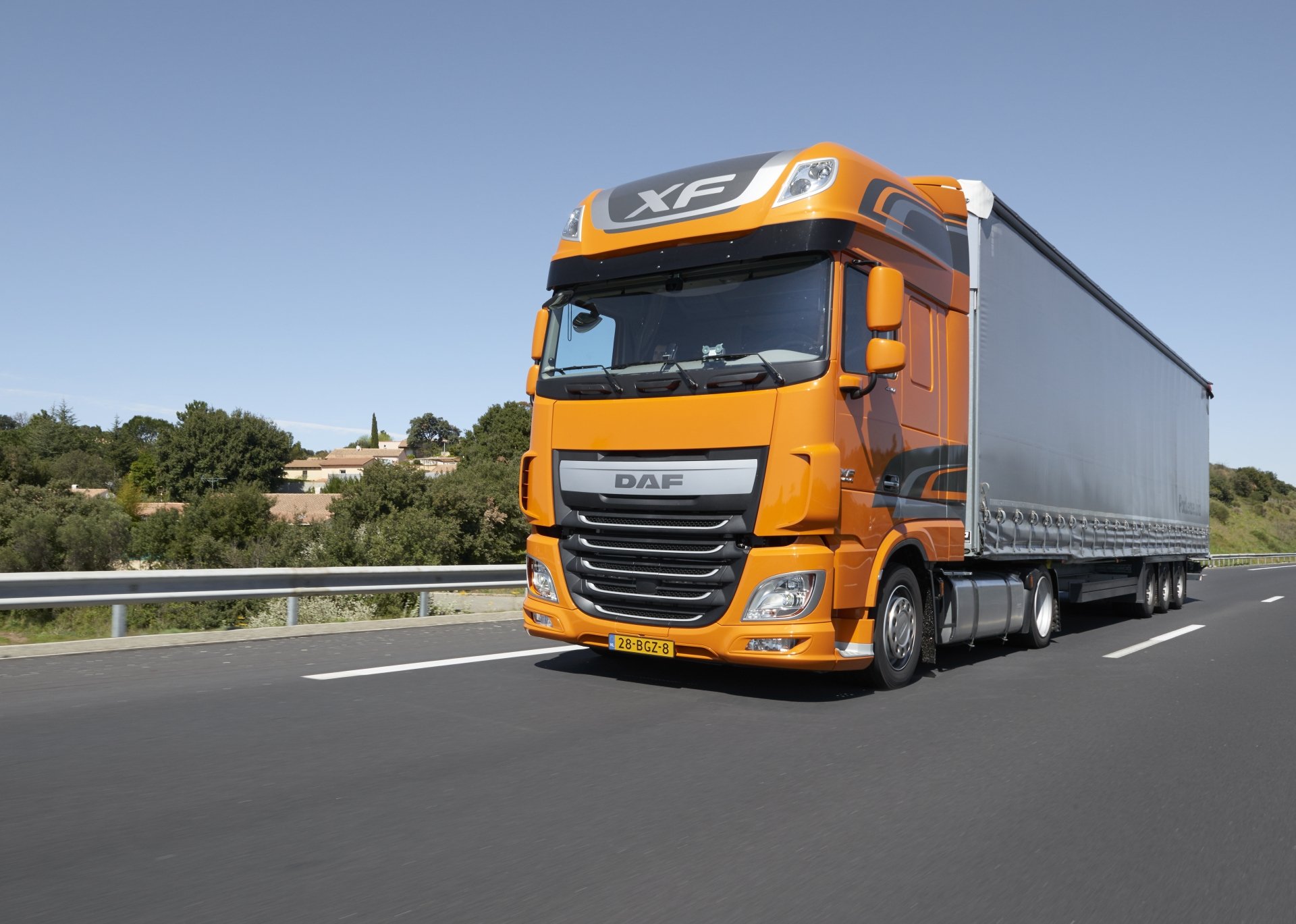 8K Ultra HD wallpaper featuring an orange DAF XF truck driving on a highway with greenery and clear skies in the background.
