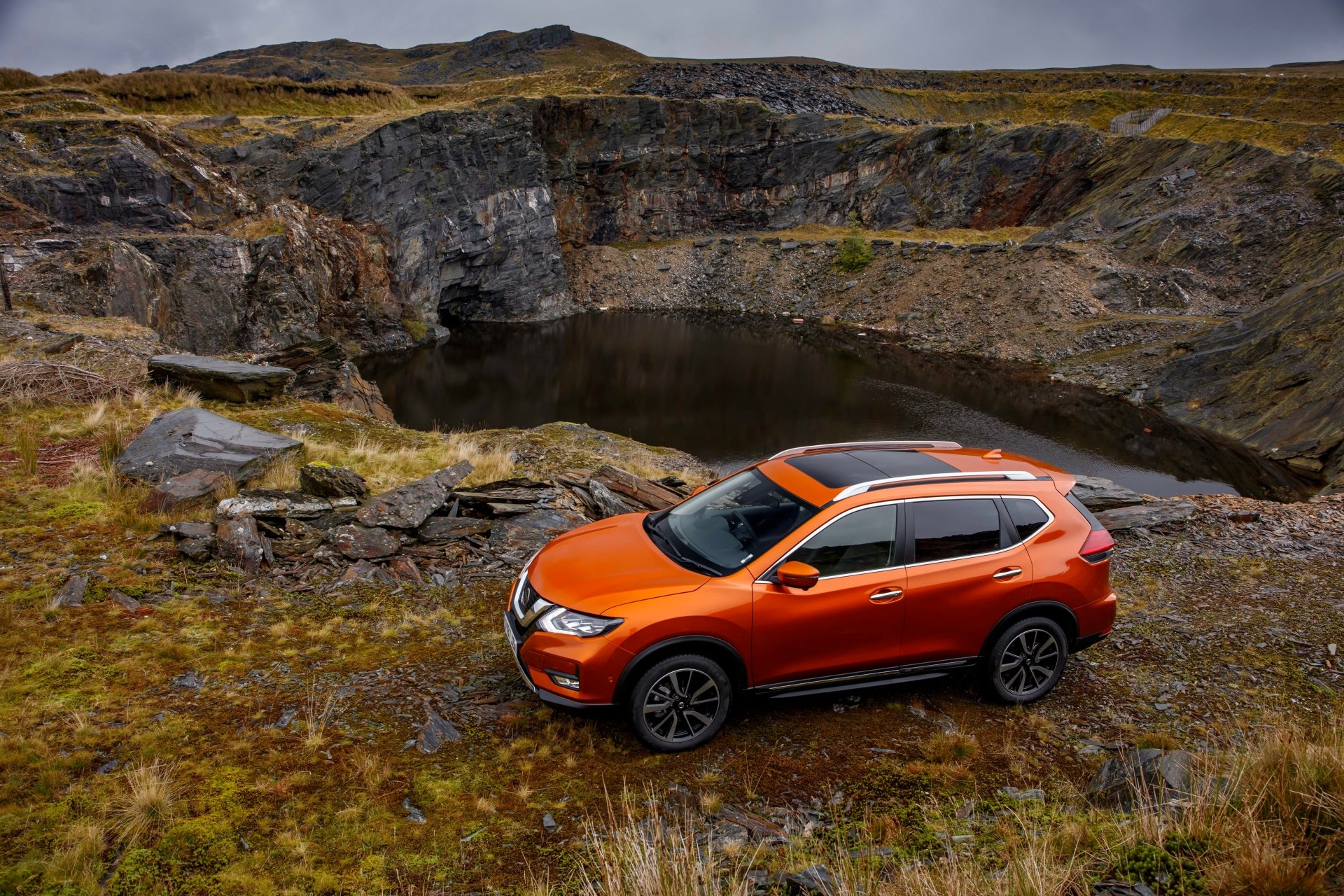 Orange Nissan X-Trail SUV parked on a rugged moor beside a rocky pond, captured as a 4K Ultra HD PC desktop wallpaper background.