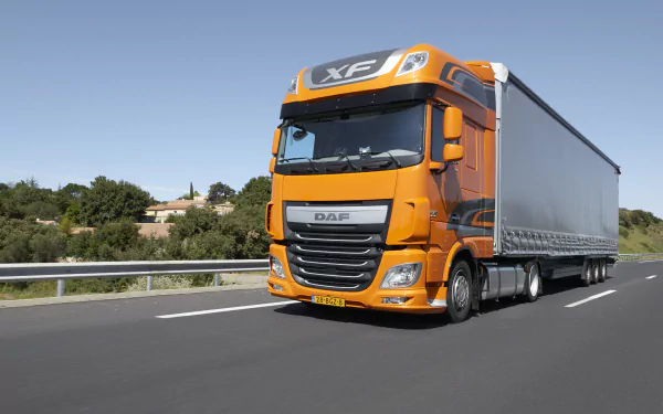 8K Ultra HD wallpaper featuring an orange DAF XF truck driving on a highway with greenery and clear skies in the background.