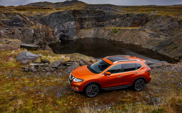 Orange Nissan X-Trail SUV parked on a rugged moor beside a rocky pond, captured as a 4K Ultra HD PC desktop wallpaper background.
