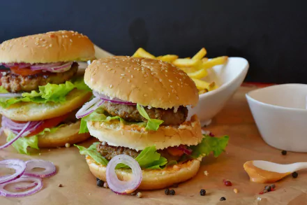 HD PC desktop wallpaper showing two juicy hamburgers with lettuce, cheese and onion rings, served with fries — a lunch meal burger food background.