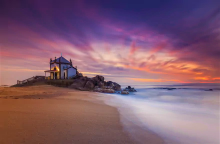 Sunset over a serene Portuguese beach with a small religious chapel perched on rocky shore, overlooking the ocean horizon in this HD desktop wallpaper.