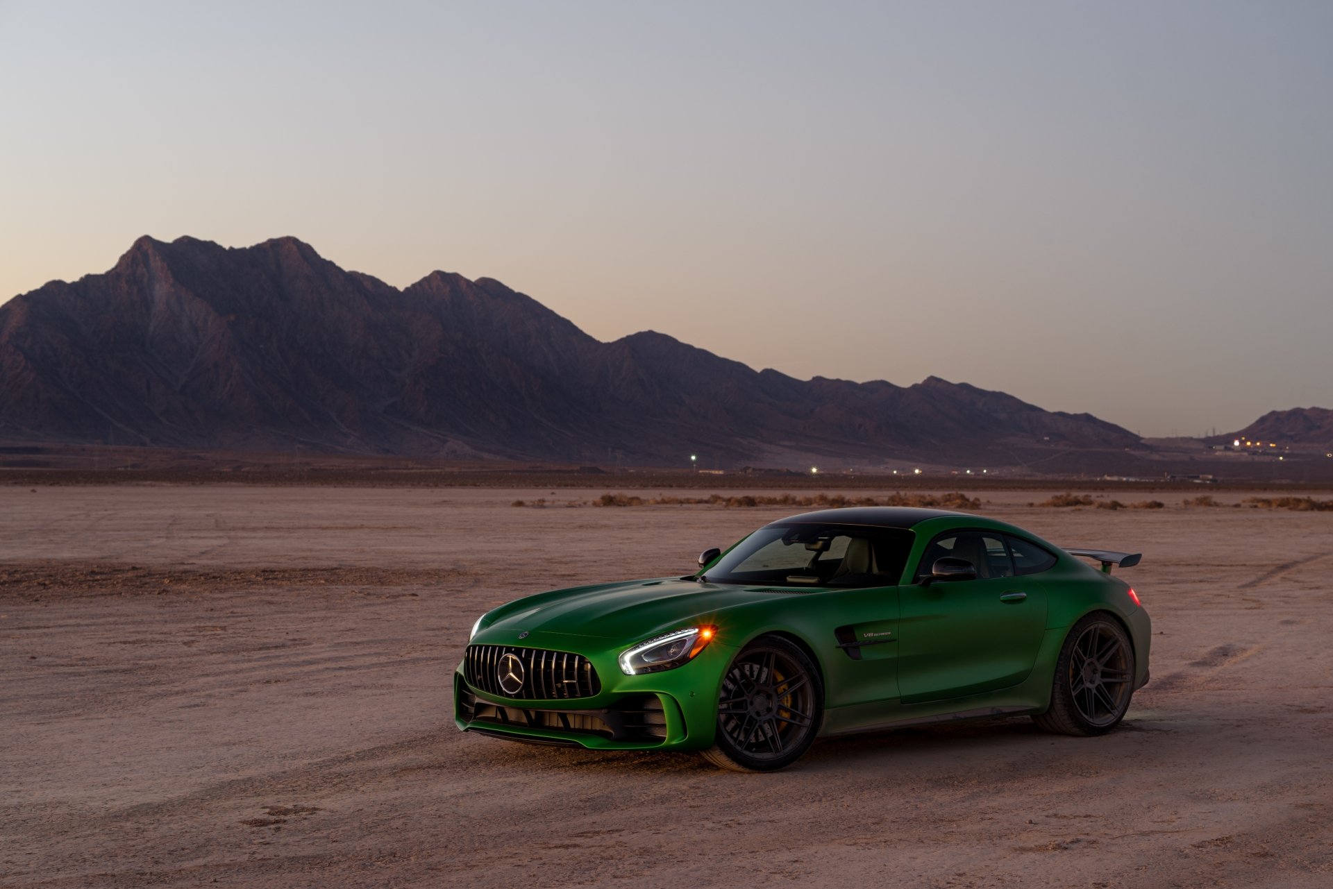 A green Mercedes-AMG GT supercar parked on a desert landscape at dusk with mountains in the background, captured in stunning 4K Ultra HD quality.