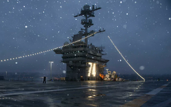 Snowfall over the USS John C. Stennis (CVN-74) aircraft carrier, showcasing the navy warship deck and military lights in an HD desktop wallpaper scene.